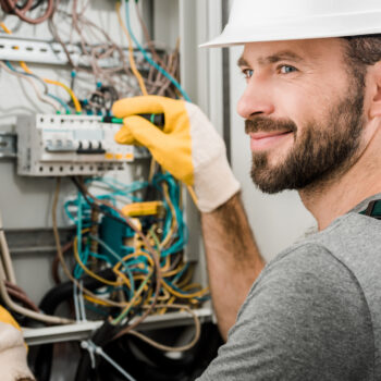 Handsome Cheerful Electrician Repairing Electrical Box and Using Screwdriver in Corridor electrical contractors near me top mistakes to avoid when hiring one