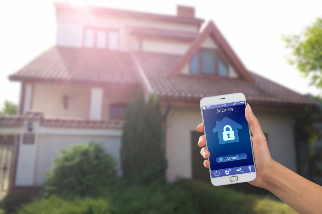 Smartphone with Home Security App in a Hand on the Building Background 5 tips for choosing an alarm system installation company