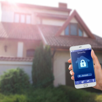 Smartphone with Home Security App in a Hand on the Building Background 5 tips for choosing an alarm system installation company